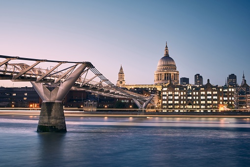 London cityscape at dusk. City waterfront with Millennium Footbridge against St. Pauls Cathedral. United Kingdom.