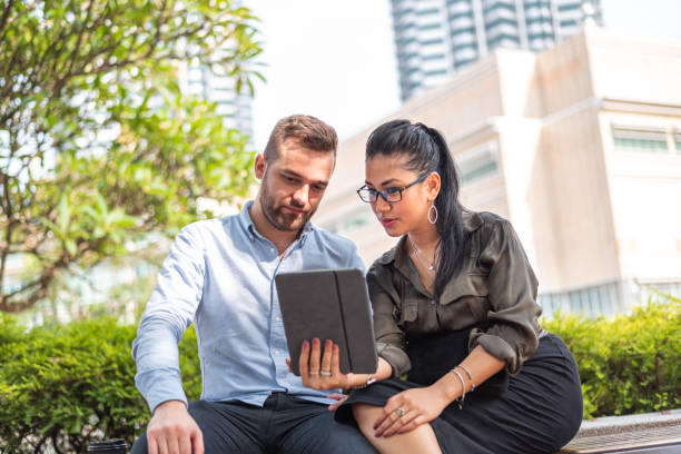 istock Young colleagues sitting on a park bench and using laptop 1312473976