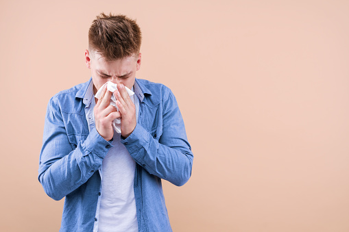 Allergy concept. Home treatment. Young sick man has runny nose. Flu and virus infection, coronavirus covid-19 symptoms. Immunity against epidemic, pandemic. Hipster blow out snot, sneezing in paper.