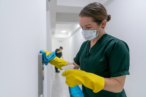 Portrait of a Latin American cleaner wearing a facemask while cleaning the buttons of an elevator at an office building during the COVID-19 pandemic