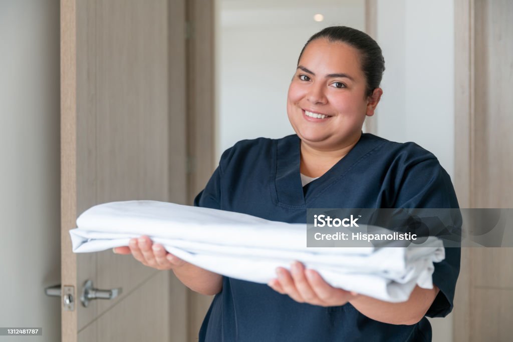 Happy cleaner working at a hotel and changing the towels in a room Portrait of a happy Latin American cleaner working at a hotel and changing the towels in a room while looking at the camera smiling Housekeeping Staff Stock Photo