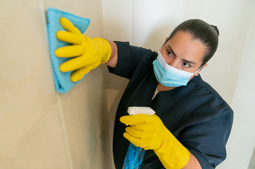 Portrait of a Latin American cleaner wearing a facemask while cleaning the tiles of an office building during the COVID-19 pandemic