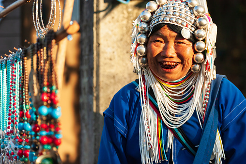 Chiang Rai, Thailand - December 3, 2014: An elder Akha woman in traditional clothing selling Akha traditional souvenir handmade, accessories, necklace, silver and bead at local market. Doi Mae Salong.