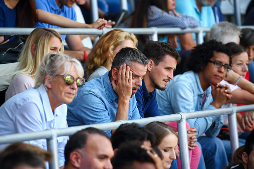 Man with hand on head in a crowd of spectators on a sports match. Soccer, american football, baseball spectators sad on stadium.