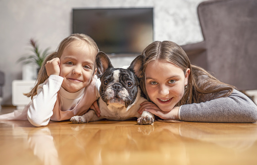 Home portrait of two cute children, sisters hugging with puppy on the floor