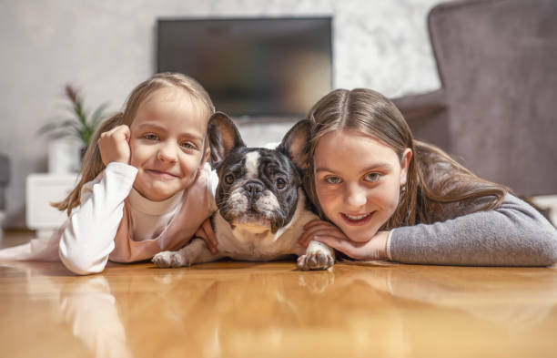 domowy portret dwojga uroczych dzieci, sióstr przytulających się ze szczeniakiem na podłodze - pets baby young animal child zdjęcia i obrazy z banku zdjęć