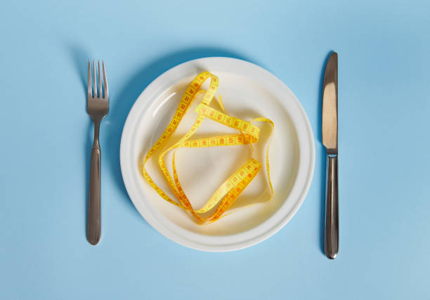 istock Knife, fork and measuring tape on an empty plate. Diet concept on blue background with copy space 1312491371