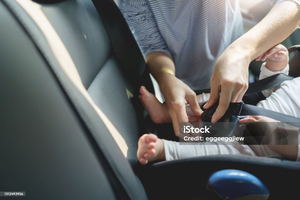 Mother fasten belt her little newborn baby in car seat for safety in transportation before traveling on road trip Mother fasten belt her little newborn baby in car seat for safety in transportation before traveling on road trip. Car Safety Seat Stock Photo