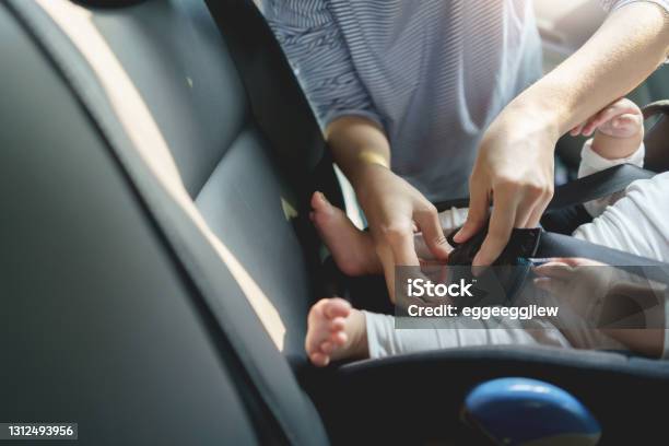 Mother Fasten Belt Her Little Newborn Baby In Car Seat For Safety In Transportation Before Traveling On Road Trip Stock Photo - Download Image Now