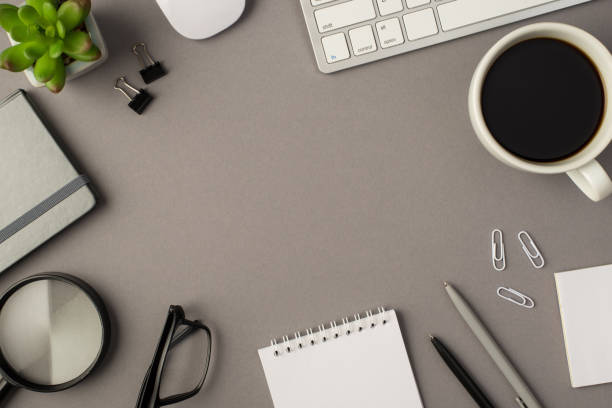 istock Overhead photo of empty notebook keyboard computer mouse magnifier pens phone plant glasses cup of coffee and paperclips isolated on the grey background with empty space 1312495246