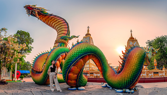 Rainbow carve serpent or colorful Thai Naga and asian woman standing in the sunset at Wat Phra That Nong Bua temple, Ubon Ratchathani