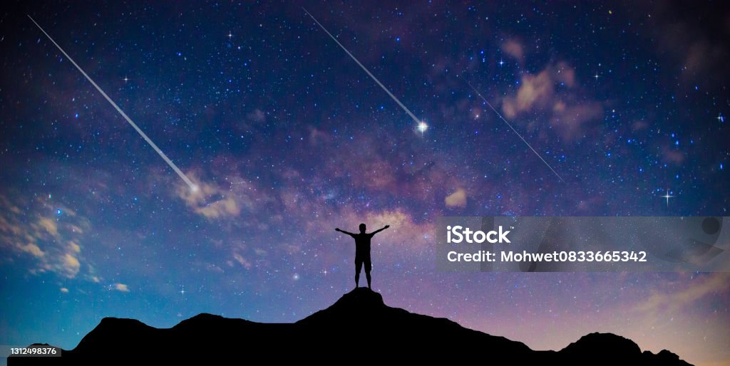 Amazing beautiful night sky and stars with meteor or shooting star as background.Traveler Man Silhouette Stand Top Mountain. Meteor Stock Photo