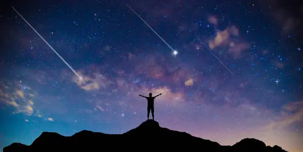 Photo of Amazing beautiful night sky and stars with meteor or shooting star as background.Traveler Man Silhouette Stand Top Mountain.