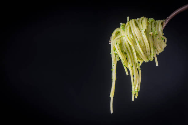 Spaghetti with green pesto sauce made with wild garlic rolled on a fork, close up. Isolated over black background