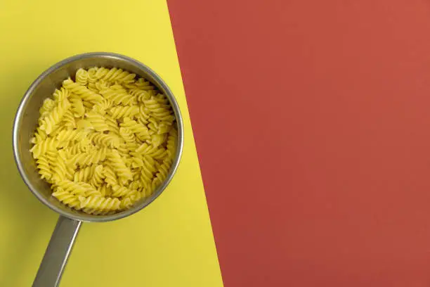 pasta in saucepan on the red-yellow background close up