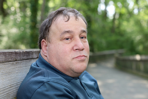 Middle aged autistic man sitting on a bench outdoors.