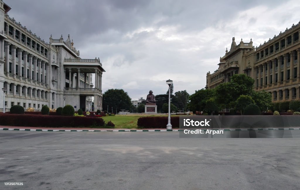 Wide angle view of Statue of Mahatma Gandhi against road, a freedom fighter known for peace and the side view of Vikasa Soudha building. Famous landmark in South Bangalore, India - September 04, 2016: Wide angle view of Statue of Mahatma Gandhi against road, a freedom fighter known for peace and the side view of Vikasa Soudha building. Famous landmark in South Architectural Dome Stock Photo