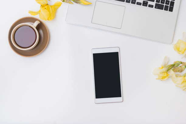 istock Flat lay home office desktop with laptop, yellow irises, cup with coffee on a white background. Top view mockup tablet with blank screen 1312508480