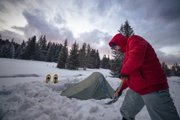 Tourist setting up tent while camping in winter mountain. Alone in nature while COVID-19 pandemic. Mental health and life balance. Man spending vacation in the nature during coronavirus pandemic. Setting his tent up after a long hiking day. snowshoeing snow shoe red stock pictures, royalty-free photos & images