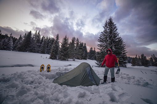 Man spending vacation in the nature during coronavirus pandemic. Setting his tent up after a long hiking day.