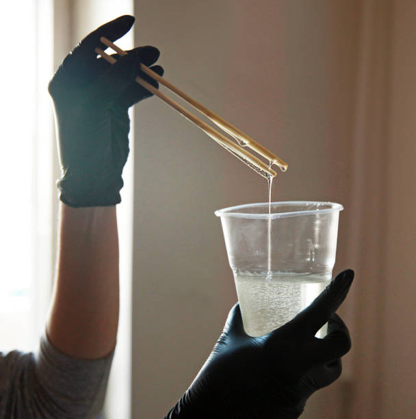 resina epossidica, una ragazza con guanti mescola scrupolosamente il liquido in una tazza di plastica, contro la finestra. - paint mixing stick foto e immagini stock