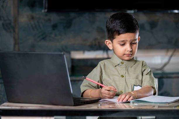 kleiner junge, der online-kurse auf laptop besucht und zu hause auf notebook schreibt. - reading and writing little boys reading asian ethnicity stock-fotos und bilder