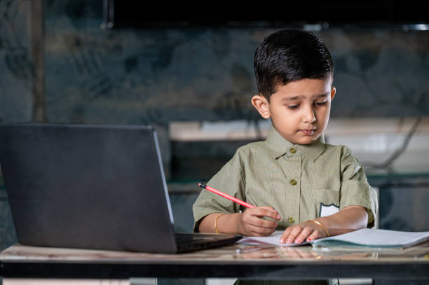 маленький мальчик, посещающий онлайн-классы по ноутбуку и пишущий на ноутбуке дома. - reading and writing little boys reading asian ethnicity стоковые фото и изображения