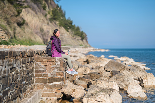 Young asian woman is sitting on coastline in Slovenia. She is enjoying the sun.