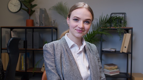 Joyful girl entrepreneur freelancer concentrated developing new project while looking at camera. Young businesswoman boss working in modern office interior. Portrait of positive woman co-worker