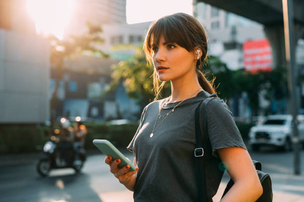 молодая женщина, глядя на улице холдинг телефон - beautiful one person contemplation surprise стоковые фото и изображения