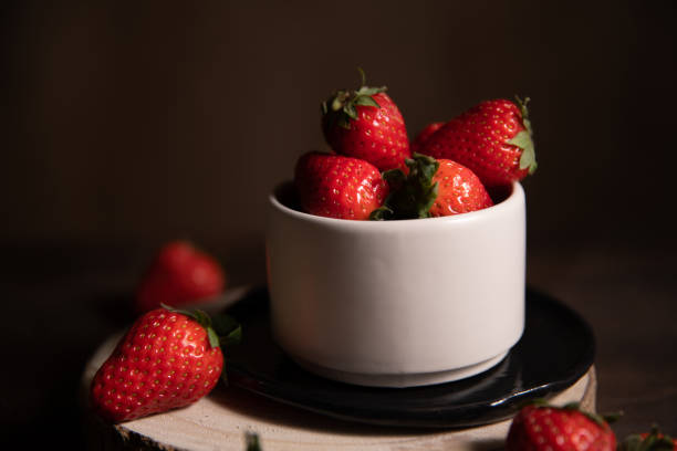 istock Ripe garden strawberries in white ceramic bowl on dark table. 1312530496