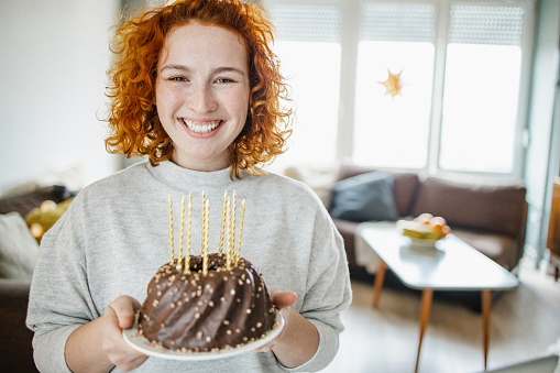 A young woman is in the living room, she is holding a birthday cake