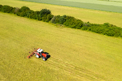 Aerial view of an agricultural field with a tractor with rotary hay rake, designed to fluff up the hay and turn it over so that it may dry during hay harvest.