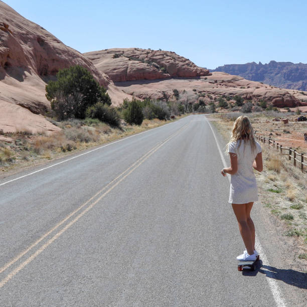 Young woman skateboards along desert road in the morning She looks off towards desert and mountain ranges in the distance single yellow line sunlight usa utah stock pictures, royalty-free photos & images