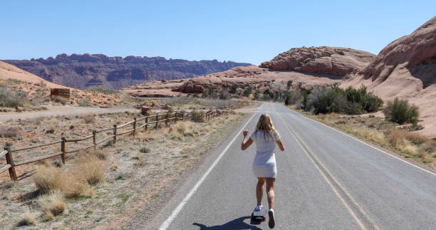 Young woman skateboards along desert road in the morning She looks off towards desert and mountain ranges in the distance single yellow line sunlight usa utah stock pictures, royalty-free photos & images