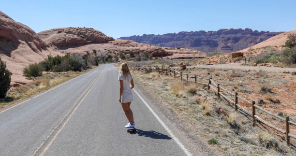 Young woman skateboards along desert road in the morning She looks off towards desert and mountain ranges in the distance single yellow line sunlight usa utah stock pictures, royalty-free photos & images