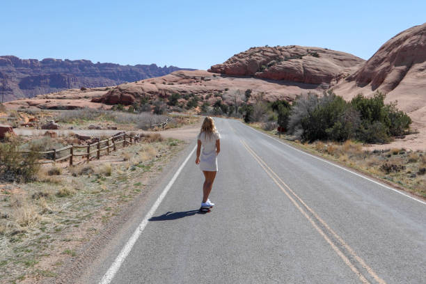 Young woman skateboards along desert road in the morning She looks off towards desert and mountain ranges in the distance single yellow line sunlight usa utah stock pictures, royalty-free photos & images