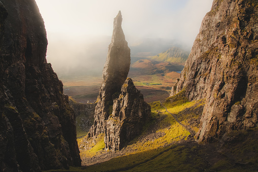 Moody, atmospheric fog and mist with golden sunrise or sunset light and shadow at the iconic Needle rock pinnacle at the Quiraing on the Trotternish Ridge, Isle of Skye.