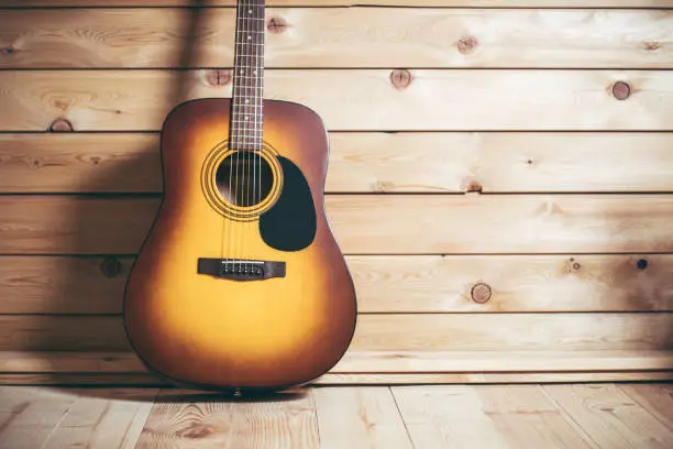 Acoustic six-stringed yellow-brown guitar standing near wooden wall, copy space.