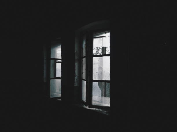 istock Scary windows. Inside an abandoned house. View of broken windows without a curtain. Grunge scene. Light shines through old wooden frames with broken glass. The concept of abandonment and uselessness 1312551672