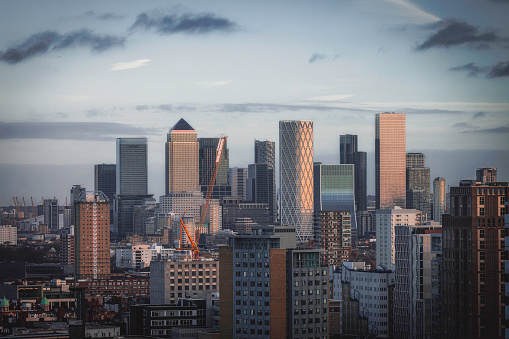 Aerial panoramic view of The City of London cityscape skyline with metropole Canary Wharf financial district modern skyscrapers during sunrise with illuminated buildings and cloudy sky in London, UK