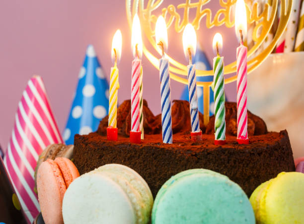 istock Fresh chocolate delicious birthday cake with macaroons and hats around it on table against pink background. Happy birthday. Close up. 1312561052