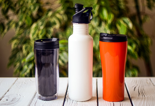 Assortment of reusable plastic and stainless steel water bottles on table against blurred background. Cut down on your plastic use concept