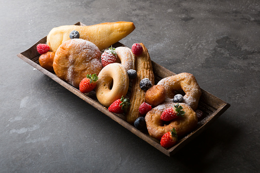 Different types of donuts served with berries on wooden tray