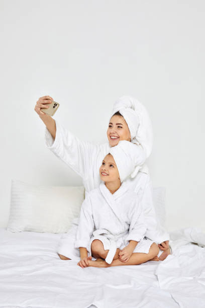 madre e hija en bata de baño tomando selfie por teléfono inteligente - little girls women red bathroom fotografías e imágenes de stock