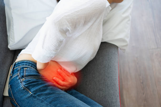 unhappy asian woman sitting on the sofa and holding on stomach suffering. abdominal pain that comes from menstruation, diarrhea, or indigestion. sickness and healthcare concept - colic imagens e fotografias de stock