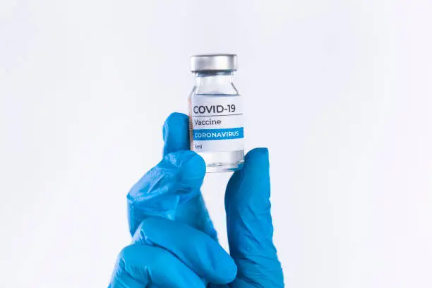 Doctor hand in protective glove holds Coronavirus Covid-19 Vaccine glass bottle. Coronavirus 2019-nCoV concept