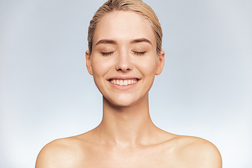 Frontal portrait of a young smiling girl with closed eyes. Face close-up of a blonde girl with bright emotions. Skin and body care concept.