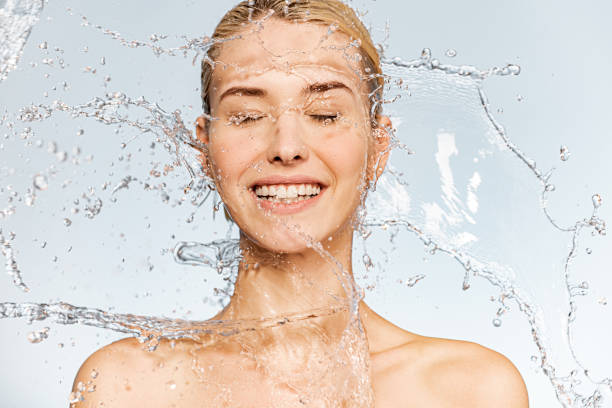 foto de una joven con la piel limpia y salpicaduras de agua. retrato de una mujer sonriente con gotas de agua alrededor de su rostro. tratamiento de spa. chica lavando su cuerpo con agua. agua y cuerpo. - human face water washing women fotografías e imágenes de stock