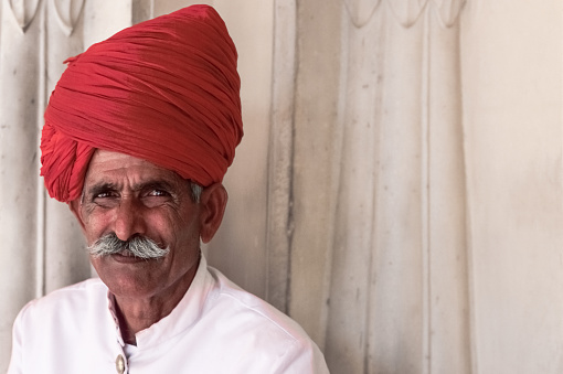 Portrait of an official doorman in white uniform and red turban at the City Palace in the Indian city of Jaipur. Horizontal composition, copy space.